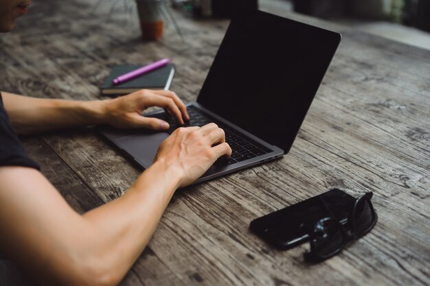 laptop em uma mesa de madeira, mãos de um homem que trabalha em um computador