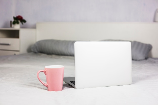 Laptop na cama branca com xícara de café