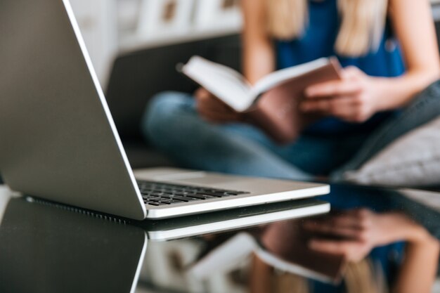 Laptop na mesa perto de mulher lendo livro em casa