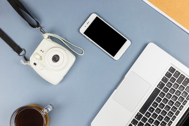 Laptop perto de smartphone, câmera e copo de bebida