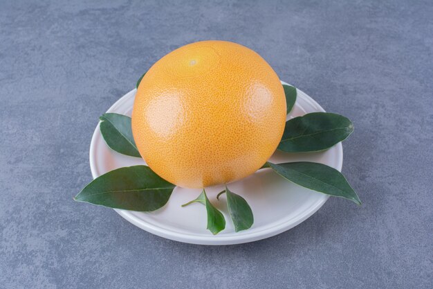 Laranja madura e suculenta com folhas no prato na superfície escura