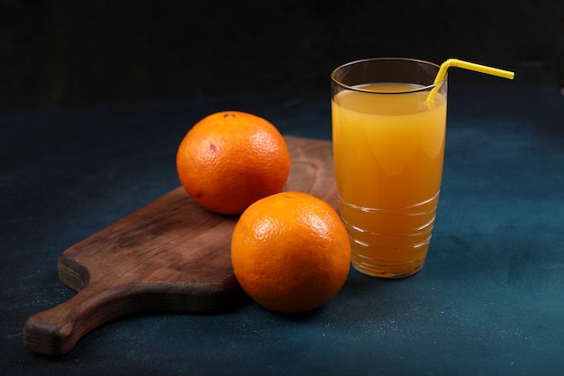 Laranjas em uma placa de madeira com um copo de suco. Fundo preto.