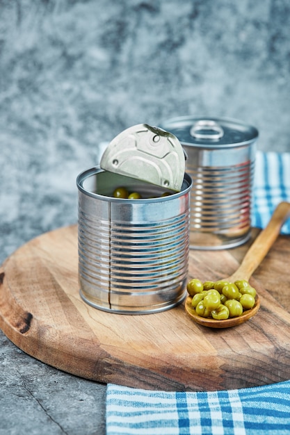 Latas de ervilhas cozidas com uma tábua de madeira e colher.