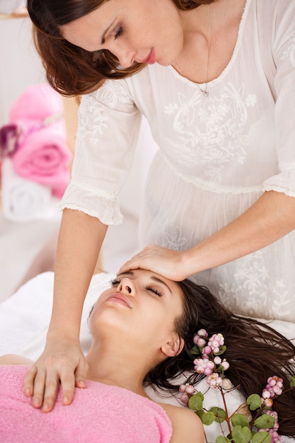 Lateral do jovem massagista fazendo massagem facial na jovem mulher