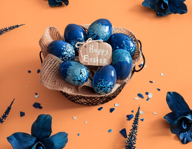 Layout de Páscoa criativo feito de ovos coloridos e flores sobre fundo azul. Conceito liso leigo da coroa do círculo. O conceito de férias da Páscoa.