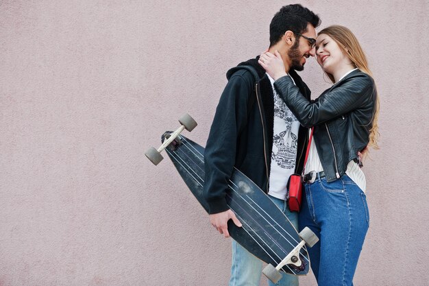 Foto grátis legal casal multirracial posando contra parede rosa com longboard