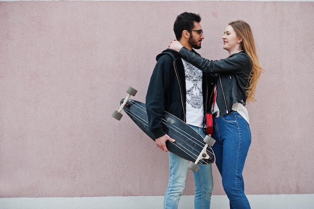 Legal casal multirracial posando contra parede rosa com longboard