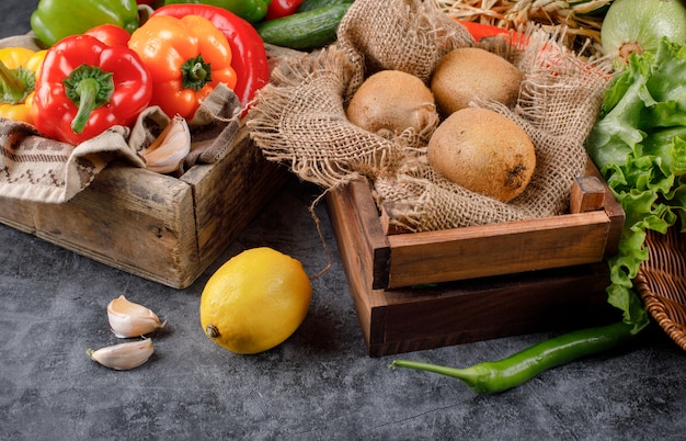 Legumes e kiwies em uma bandeja de madeira com limão e alhos ao redor.