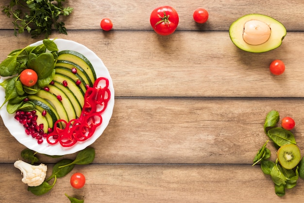 Legumes frescos e salada de frutas em chapa branca na mesa de madeira