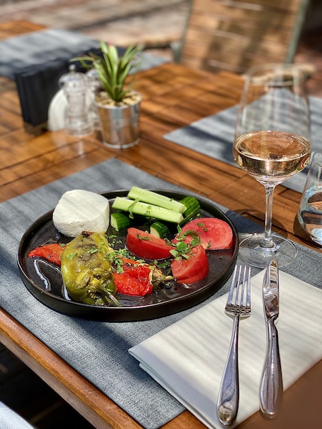 Foto grátis legumes frescos servidos em prato preto, com garfo, faca e uma taça de vinho rosé