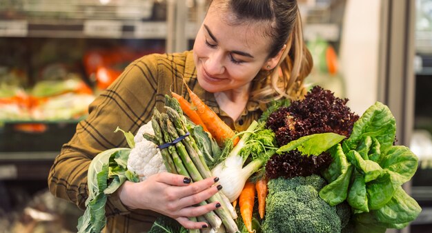 Legumes orgânicos close-up. Mulher jovem e bonita às compras em um supermercado e comprar legumes orgânicos frescos