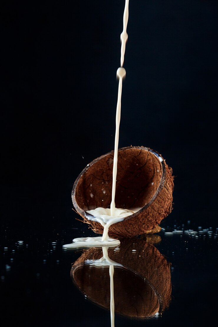 Foto grátis leite derramando metade de coco sobre a parede preta