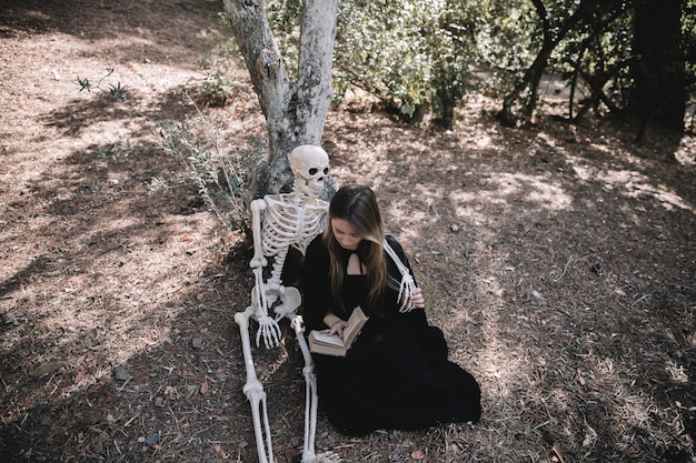 Foto grátis leitura, senhora, em, bruxa, roupas, abraçando, esqueleto