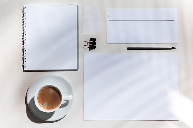 Lençóis, café, ferramentas de trabalho em uma mesa branca dentro de casa. Local de trabalho criativo e aconchegante no escritório em casa, simulação inspiradora com sombras de plantas na superfície. Conceito de escritório remoto, freelance, atmosfera.