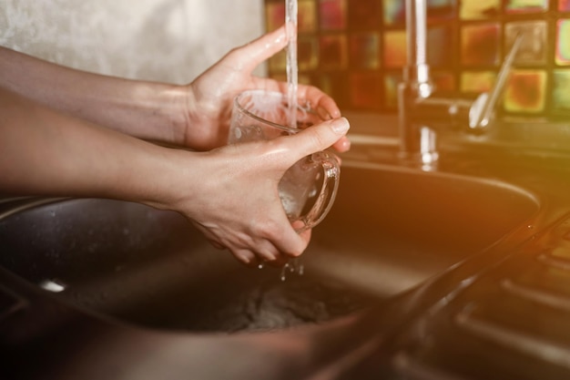 Lição de casa - close-up das mãos das mulheres lavando um copo sob um fluxo de água. tarefas domésticas