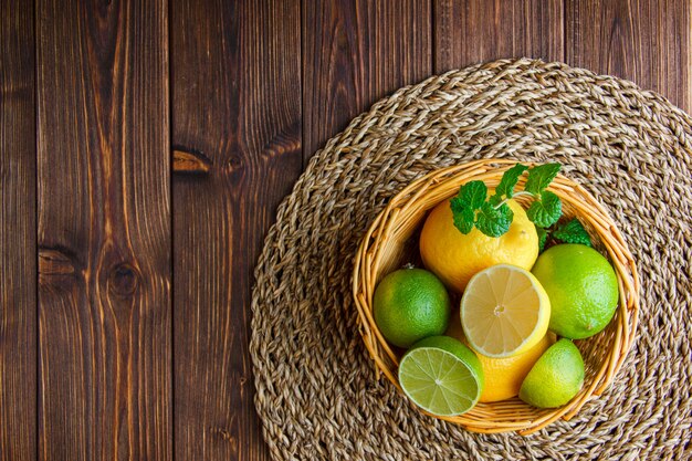 Limas com limões, ervas em uma cesta de vime na mesa de madeira