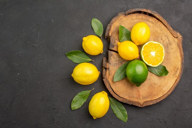 Limões azedos frescos com folhas no chão escuro, frutas e limão amarelo cítrico