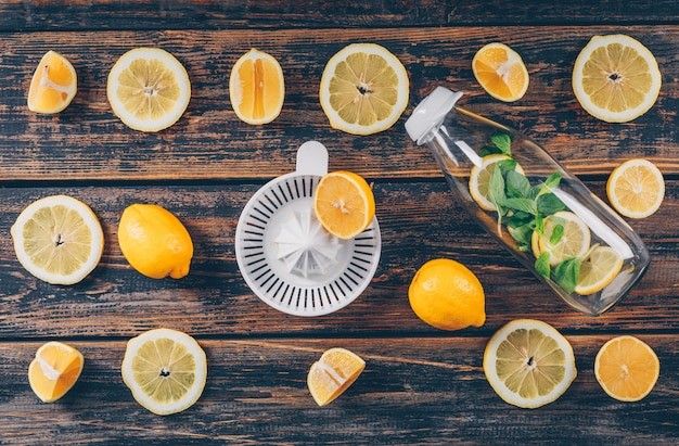 Foto grátis limões com espremedor de frutas e garrafa de vidro plana colocar sobre um fundo escuro de madeira