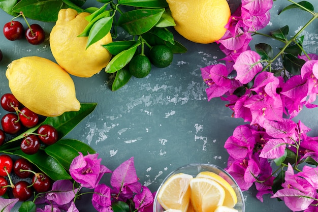 Limões com folhas, fatias, flores, cerejas na superfície de gesso