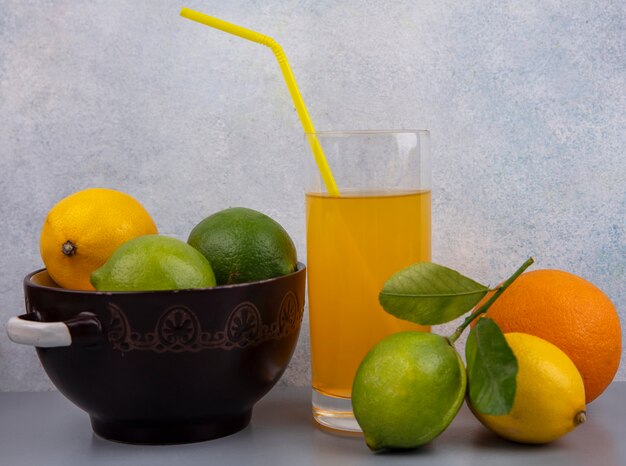 Limões com limas em uma panela com um copo de suco de laranja em um fundo cinza