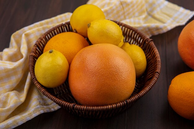 Limões de vista frontal com laranja e toranja em uma cesta com toalha amarela quadriculada em fundo de madeira