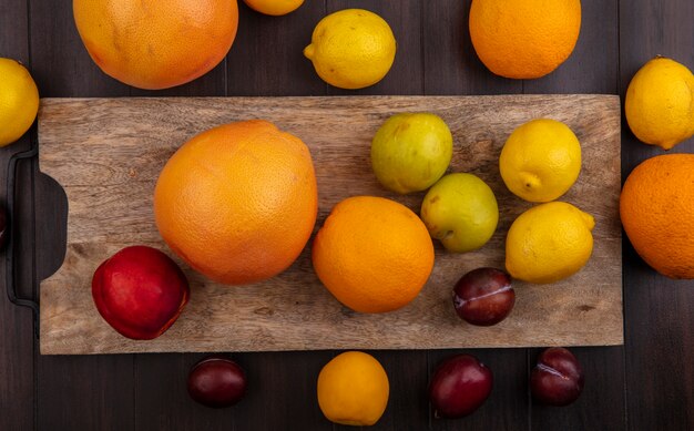 Limões de vista superior com laranjas, ameixas de pêssego e toranja em uma placa de corte em um fundo de madeira