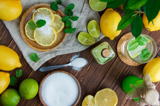 Limões em um prato com bebidas, sal, ervas, limas planas leigos na toalha de madeira e cozinha