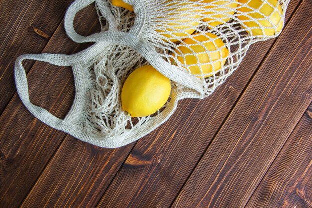 Limões em um saco de malha em uma mesa de madeira. configuração plana.