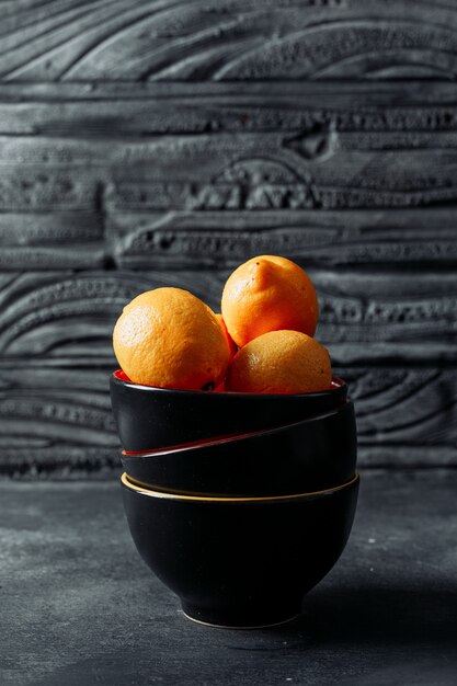 Limões em uma tigela sobre um fundo escuro de madeira. vista lateral. espaço para texto