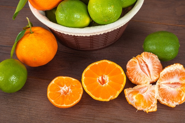 Limões verdes na cesta e tangerinas na mesa de madeira