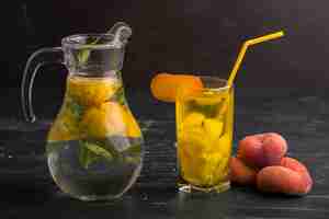 Foto grátis limonada em vidro e jarra com pêssegos isolados na superfície preta