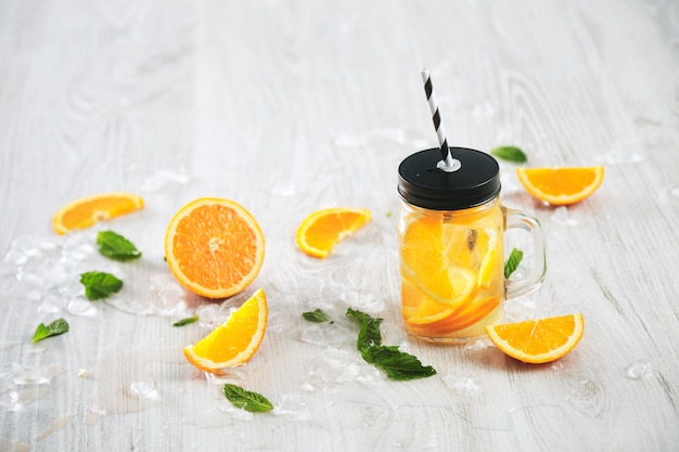 Limonada fresca de verão frio de frutas cítricas e água com gás em jarra rústica com palha de listra isolada na mesa de madeira.