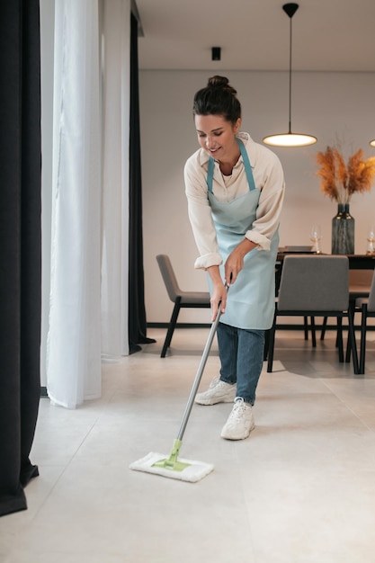 Limpando a cozinha. Uma jovem de avental limpando o chão na cozinha