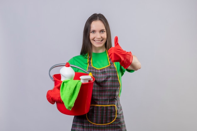 Foto grátis limpeza jovem sorridente, usando uniforme com luvas vermelhas, segurando as ferramentas de limpeza com o polegar levantado sobre fundo branco isolado