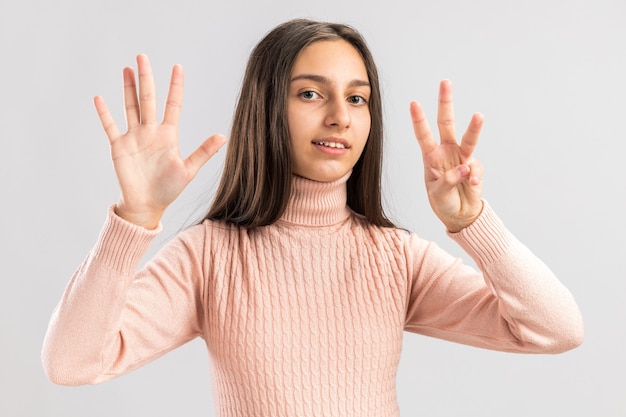 Linda adolescente sorridente olhando para a câmera que mostra o número oito com dedos isolados na parede branca com espaço de cópia