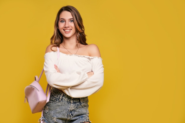 Linda aluna com uma mochila na parede amarela