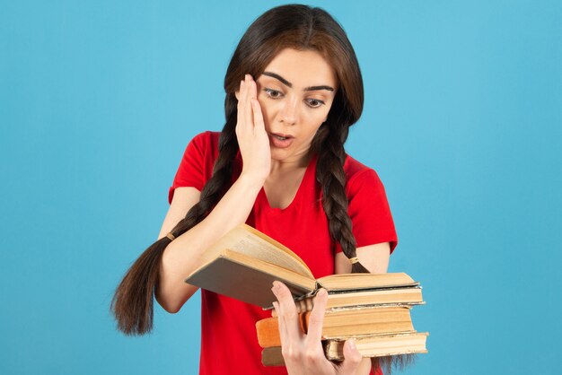 Linda aluna no livro de leitura de t-shirt vermelha com expressão de choque.