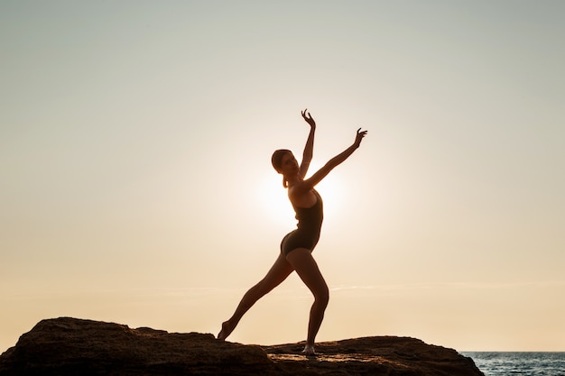 Linda bailarina dançando, posando em pedra na praia, vista para o mar.