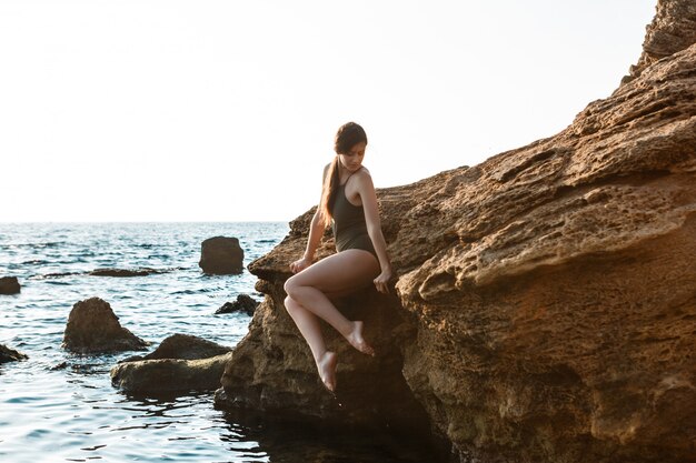 Linda bailarina dançando, posando em pedra na praia, vista para o mar.