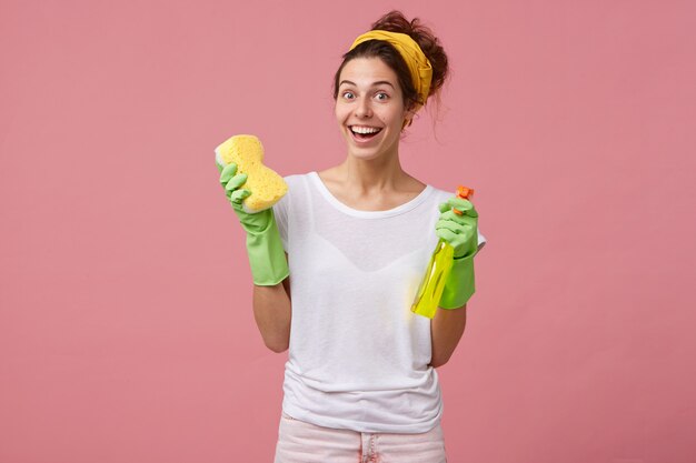 linda dona de casa com fita amarela e camiseta branca segurando o esfregão e o spray de lavar, parecendo feliz, de bom humor e deseja fazer limpeza de primavera em sua casa