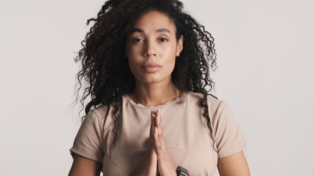 Linda e calma mulher afro inalando profundamente mostrando gesto de namaste na câmera isolada em fundo branco Garota calma