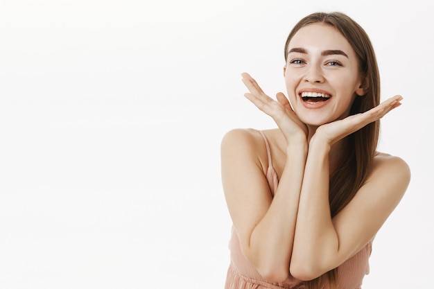 Foto grátis linda e saudável mulher encantadora com beleza natural segurando as palmas das mãos perto da linha do queixo e sorrindo amplamente satisfeita com a condição perfeita da pele, posando alegremente