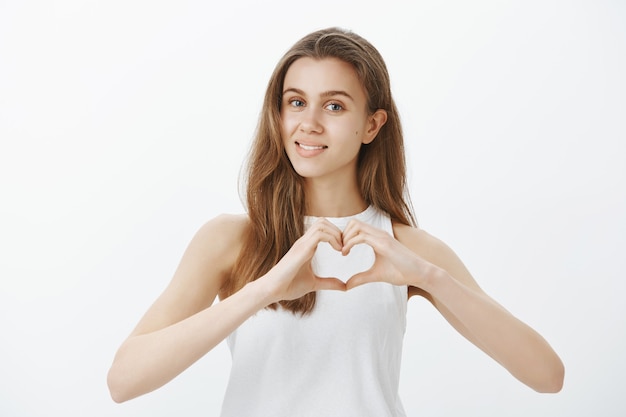 Foto grátis linda e terna jovem expressar sentimentos, mostrar simpatia, fazer um gesto de coração