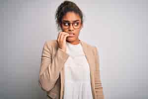 Foto grátis linda empresária afro-americana vestindo jaqueta e óculos sobre fundo branco parecendo estressada e nervosa com as mãos na boca roer unhas problema de ansiedade