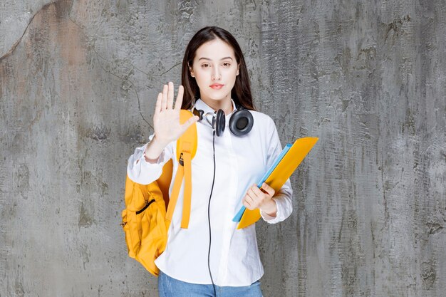 Linda estudante com mochila e fones de ouvido carregando livros. Foto de alta qualidade