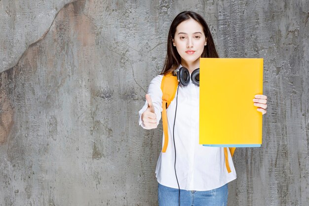 Linda estudante com mochila e fones de ouvido mostrando livros. Foto de alta qualidade