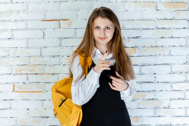 Linda estudante de uniforme fica em fundo branco e aponta o dedo para a câmera foto de alta qualidade