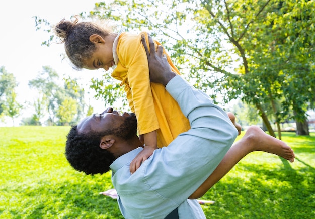 Linda família afro-americana feliz se unindo no parque - família negra se divertindo ao ar livre, pai brincando com sua linda filha Foto Premium