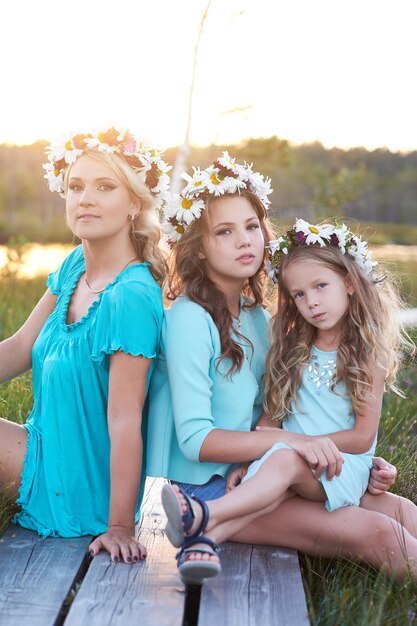 Linda família. Mãe e filhas relaxando ao ar livre enquanto está sentado em um caminho de madeira em um campo ao pôr do sol.