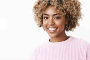 Foto grátis linda feliz aluna afro-americana com corte de cabelo loiro afro em suéter com sorriso largo alegre olhando satisfeita para a câmera com expressão despreocupada se divertindo, rindo alegremente